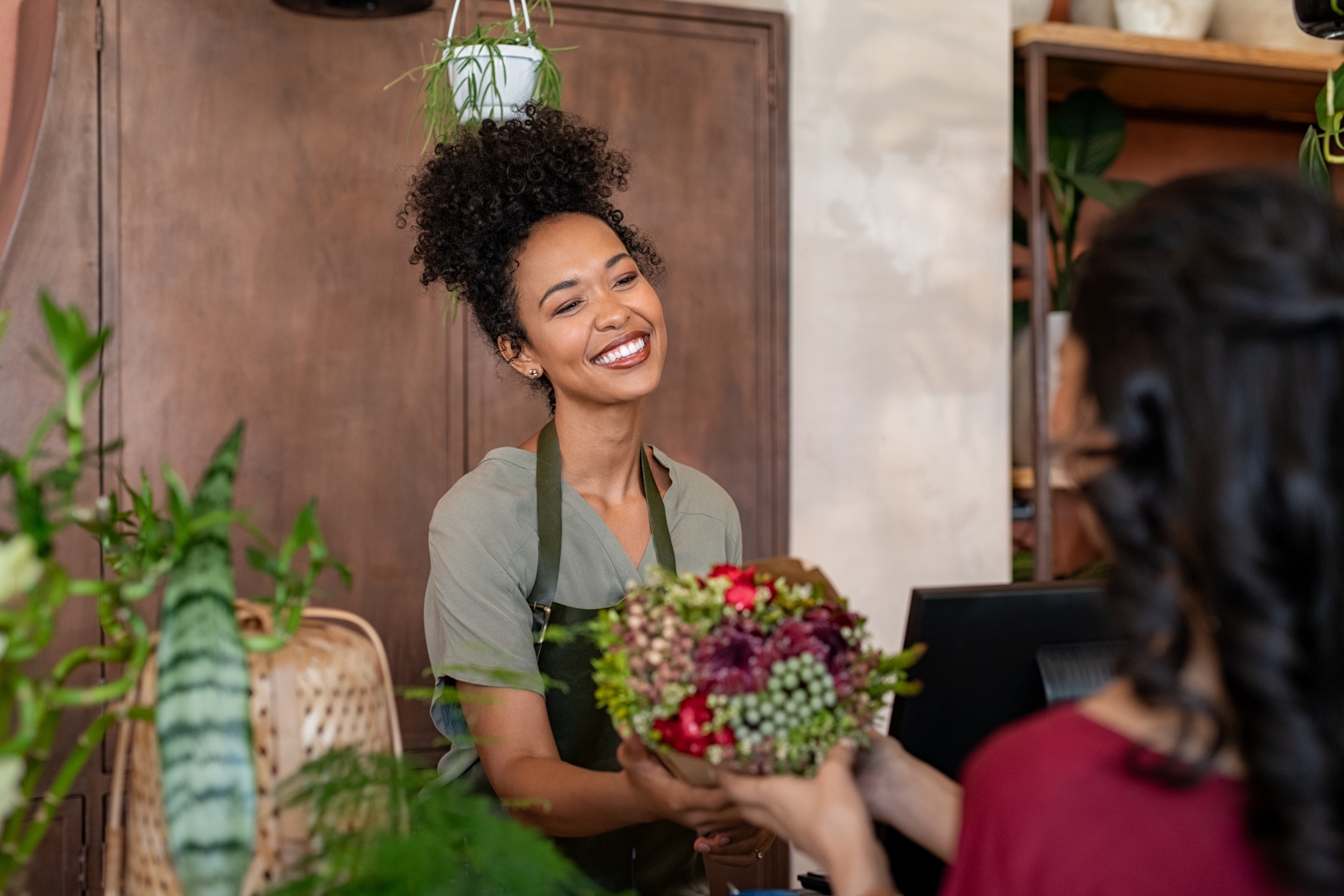 Happy black florist selling flowers to young woman