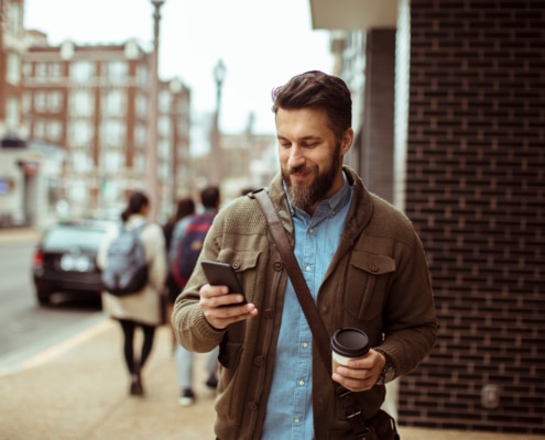 Man walking with coffee and using smartphone in city street